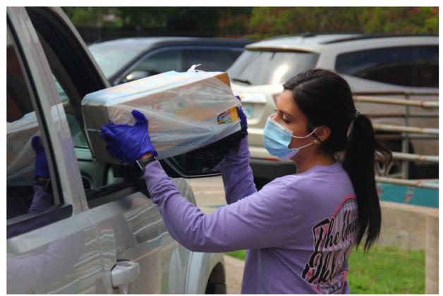 An Oklahoma City Public Schools employee wears a mask while handing food through a car window as part of the district’s meal program. (Courtesy photo)